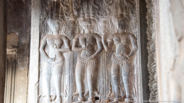 Three standing devatas in a narrow wall panel at Angkor Wat.