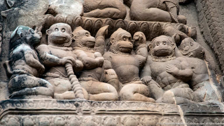 Row of expressive small figures with raised arms in a dense relief at Angkor Wat.