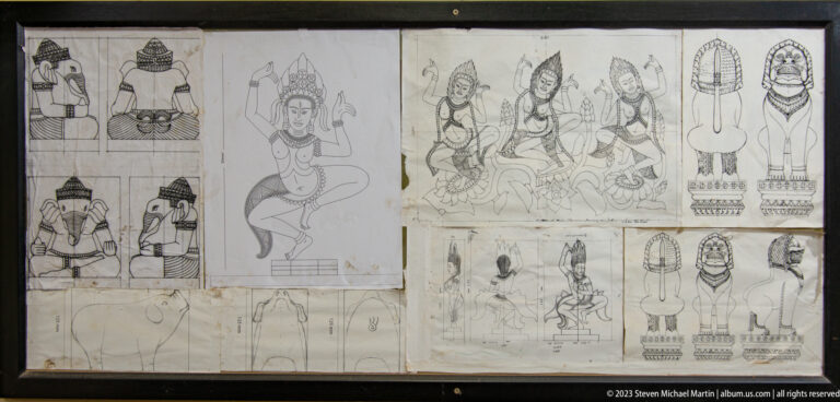 Workshop wall covered with pinned line drawings of Khmer-style figures in varied poses.
