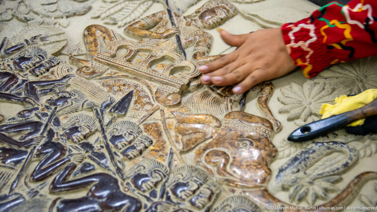 Hand rubbing a multicolored raised relief filled with figures and scrolling ornament.