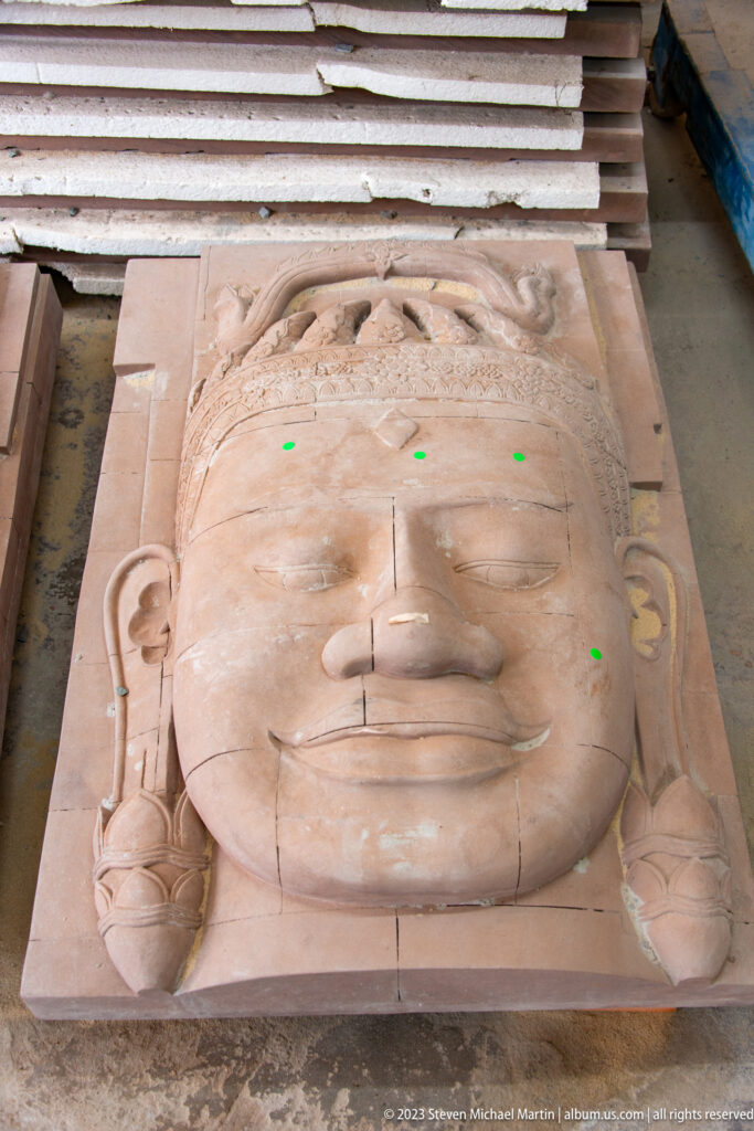 Large unfinished stone face with green reference dots, guide lines, and visible seams.