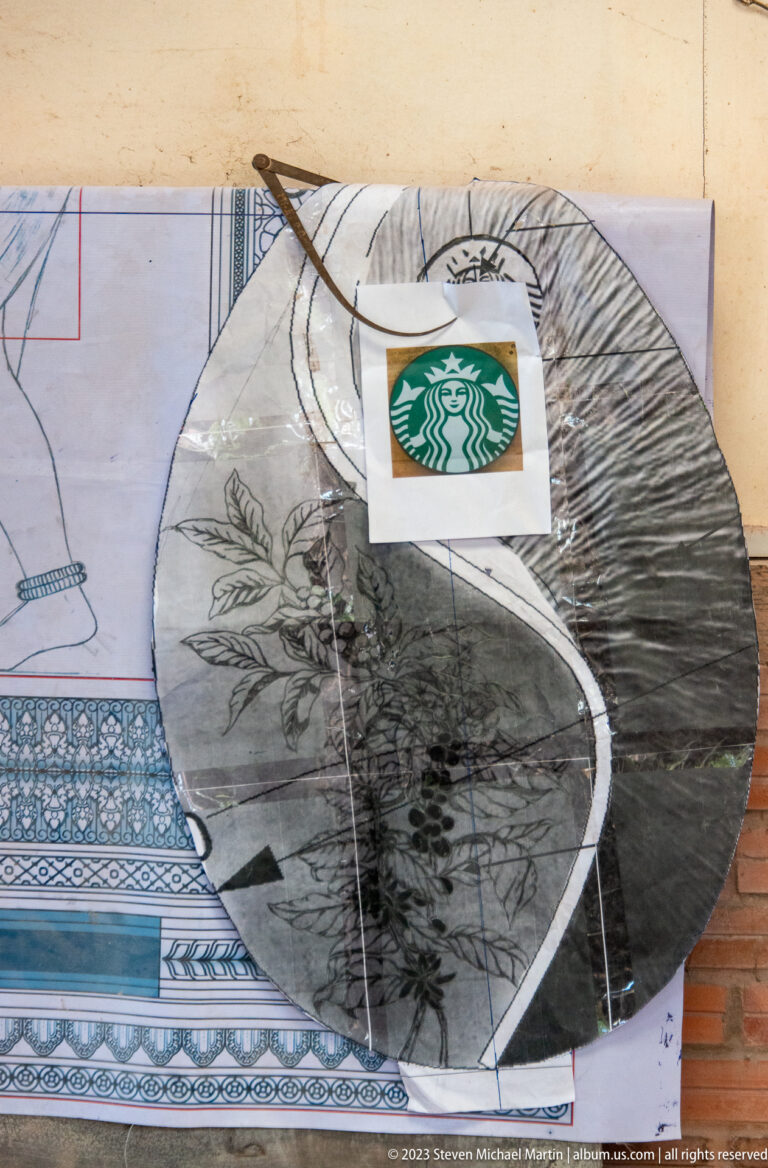 Transparent leaf-pattern tracing layered over a large drawing with a small Starbucks logo printout.