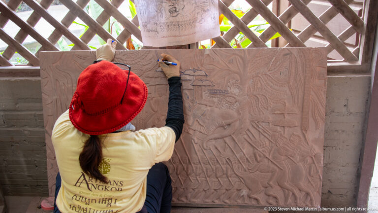 Rear view of an artisan outlining a central figure and ornament on a large relief panel.