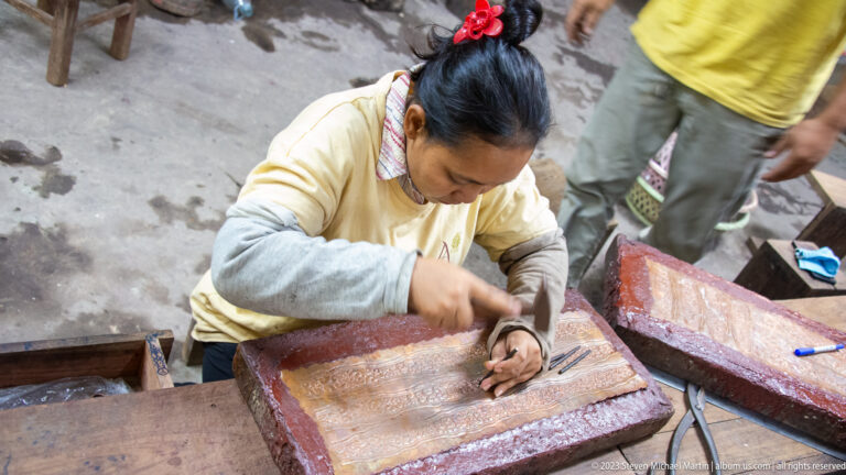 Close overhead view of a woman hammering a punch into a patterned metal sheet.