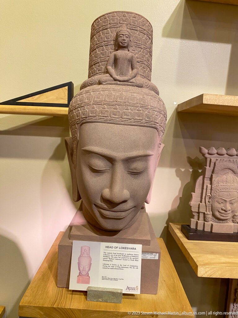 Large serene gray stone head displayed beside a smaller framed smiling-face carving.