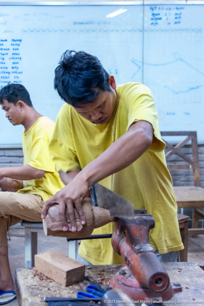 Close view of an artisan cutting a wooden block with a hand saw.