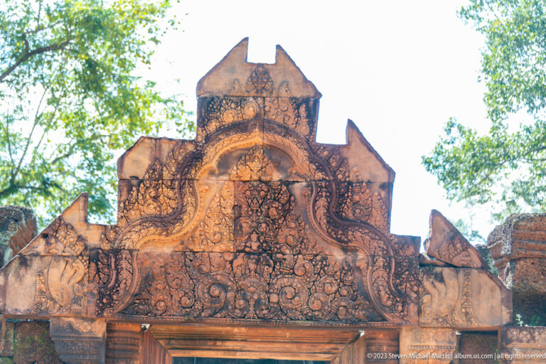 Close upward view of a densely carved pink sandstone pediment above the temple gateway.