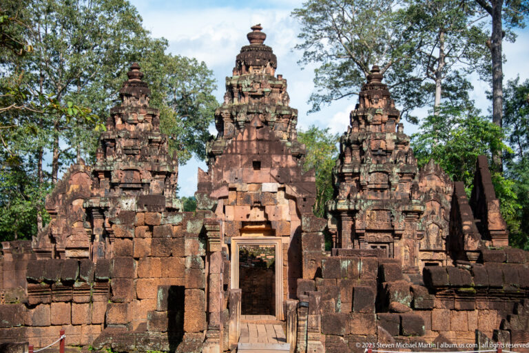 Frontal view through a sandstone doorway toward Banteay Srei's central sanctuary tower, with smaller towers on either side.