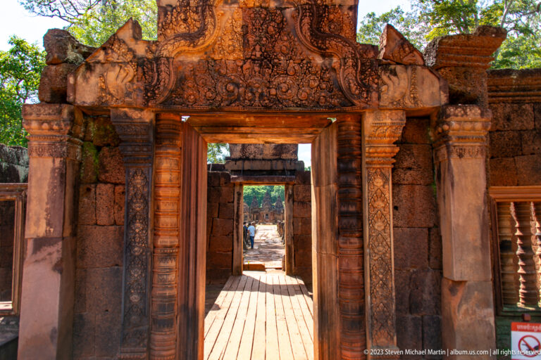 View through several aligned sandstone doorways along a wooden visitor walkway. at the Banteay Srei temple complex in Cambodia.