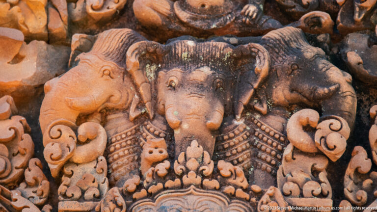 Close sandstone relief of an elephant-headed deity, likely Ganesha, framed by additional elephant heads and curling ornament.