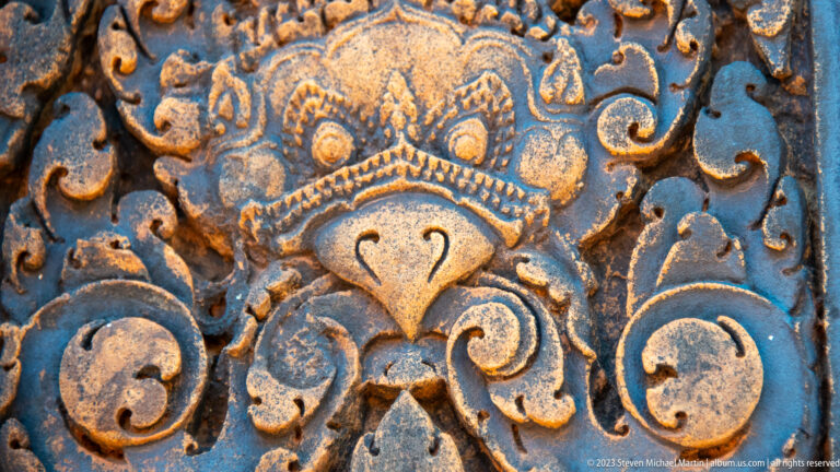 Close sandstone relief of a stylized guardian mask with round eyes, pointed lower face, and large spiral scrolls.