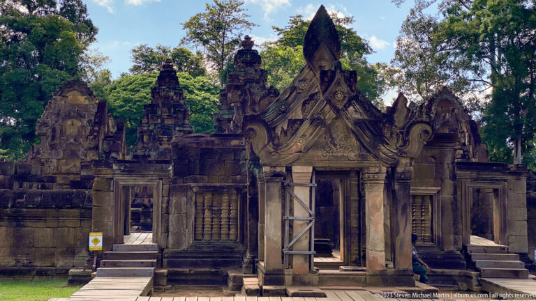 Frontal view of an ornate Banteay Srei shrine with carved pediment, balustered windows, and doorway braces.