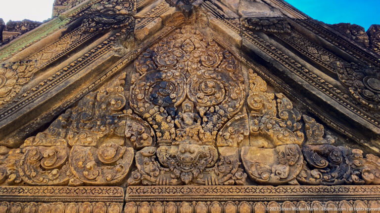 Close view of a triangular Banteay Srei pediment covered with figures, scrollwork, and monster-mask motifs.