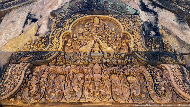 Carved Banteay Srei pediment with a seated deity above a row of attendant figures.