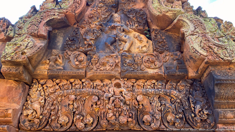 Close sandstone carving with a projecting figure, narrative band, and dense scrollwork at Banteay Srei.