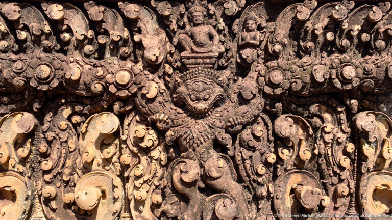 Close symmetrical relief with a winged central guardian, monster face, and dense vegetal scrollwork.