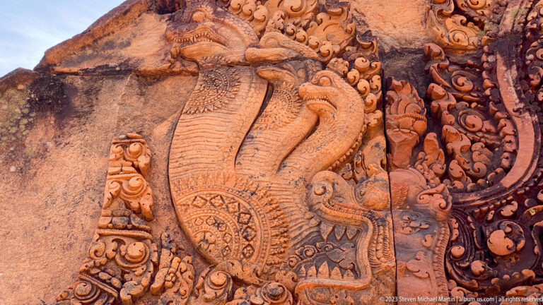 Close sandstone relief of a multi-headed naga beside a standing figure at Banteay Srei.
