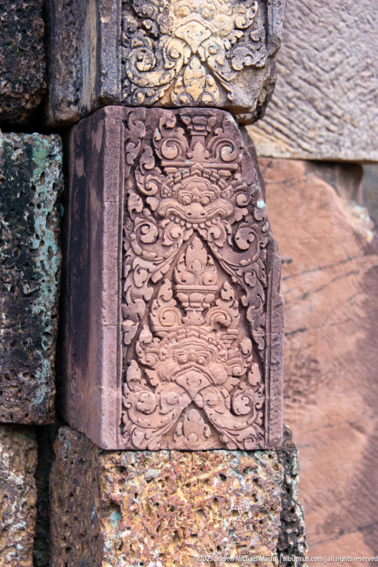 Close-up of a pink sandstone doorway jamb carved with floral scrolls and a vessel motif.
