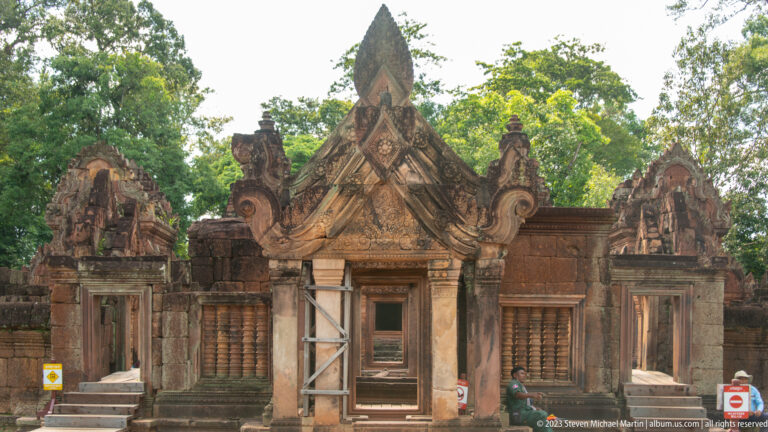 Frontal view of an ornate sandstone gateway with curled gable ends and temporary support framing.