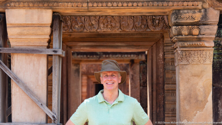 Smiling visitor in a green shirt framed by several carved sandstone doorways at Banteay Srei.