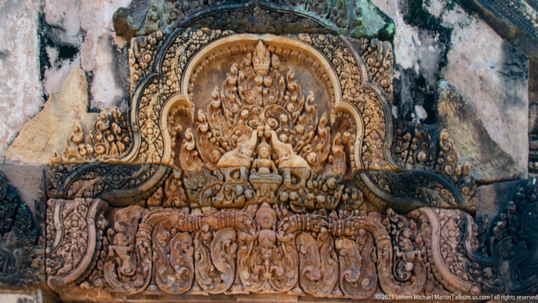 Complete arched sandstone relief with a seated figure, paired animals, and a lower row of figures.