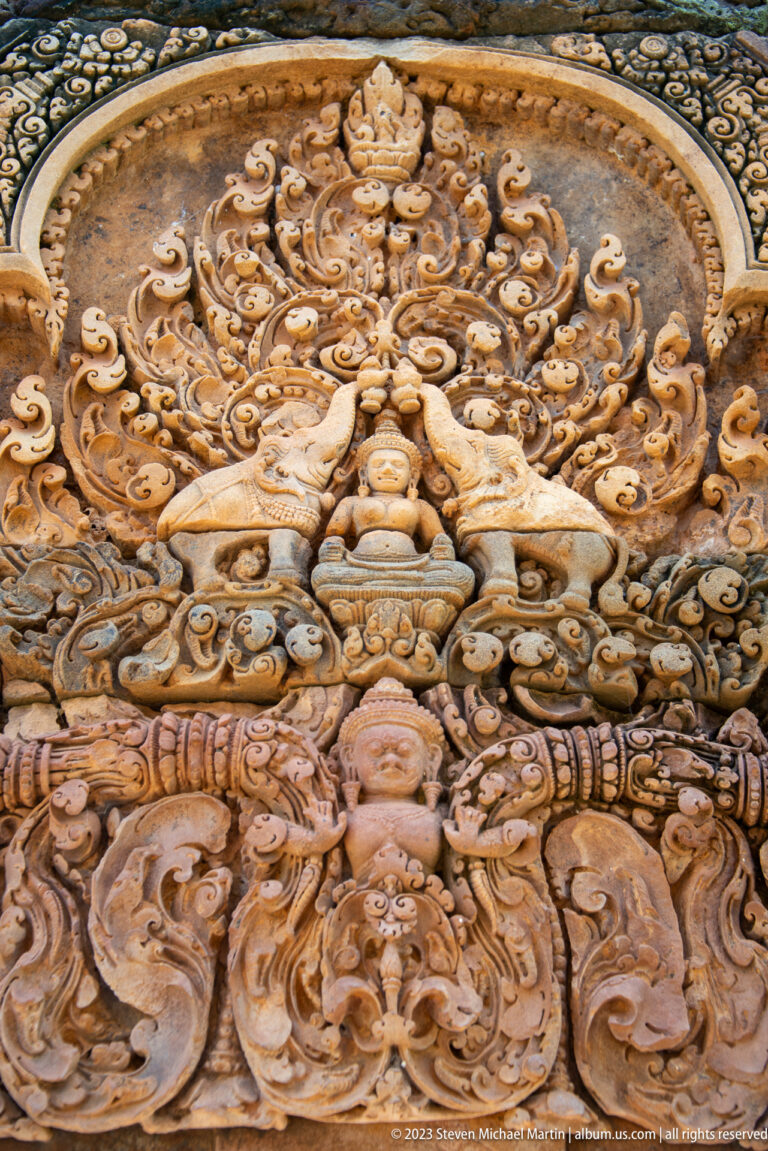 Close-up of a seated sandstone figure flanked by two animals above part of another figure.