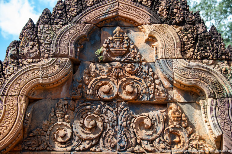Tall carved sandstone pediment with layered scrolls, cracks, and repaired sections. at the Banteay Srei temple complex in Cambodia.