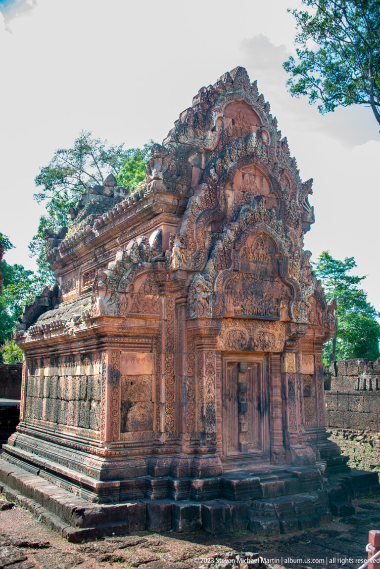 Three-quarter view of a compact pink sandstone sanctuary with an ornate carved entrance facade.