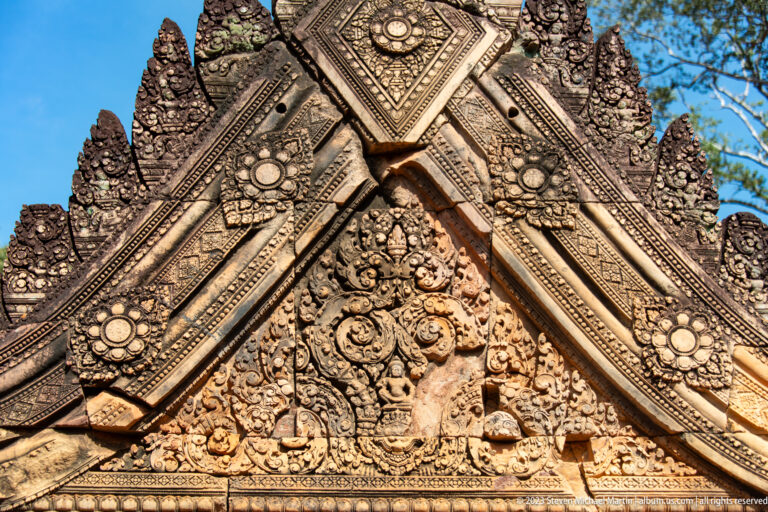 Close upward view of a pointed sandstone gable with diamond panels and floral medallions.