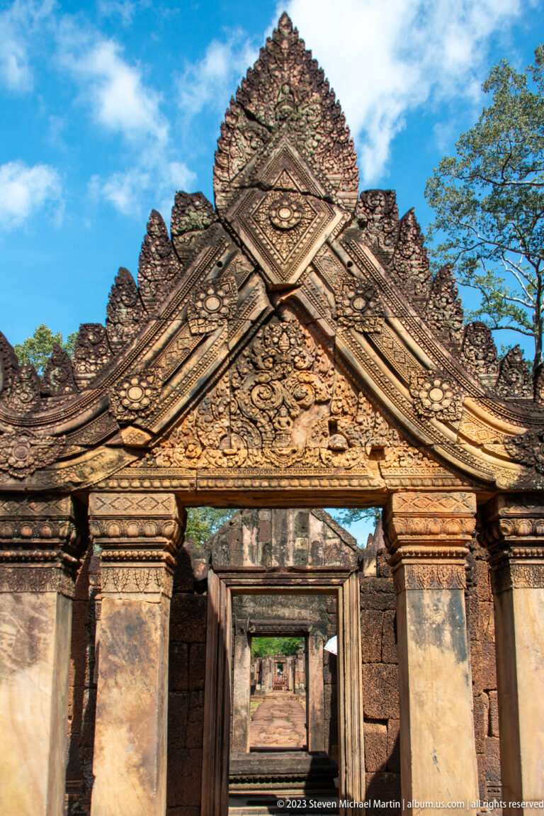 Frontal view of a complete carved sandstone gateway with pointed gable and open doorway.