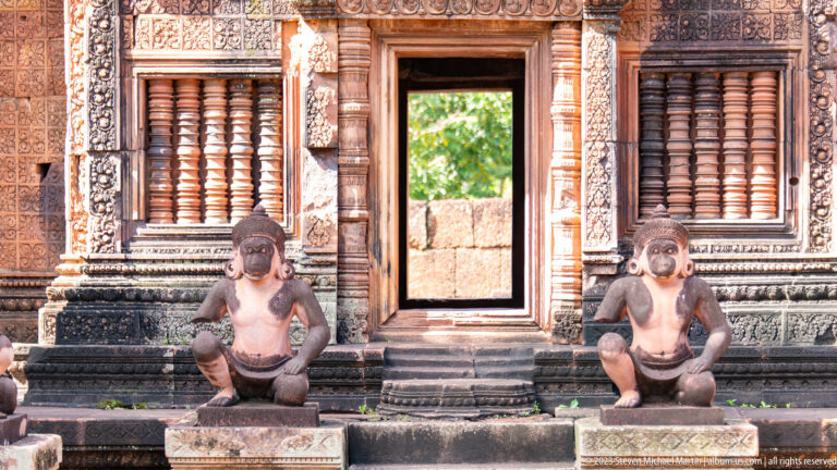 Central temple doorway flanked by two seated guardian statues and carved stone windows with vertical balusters.