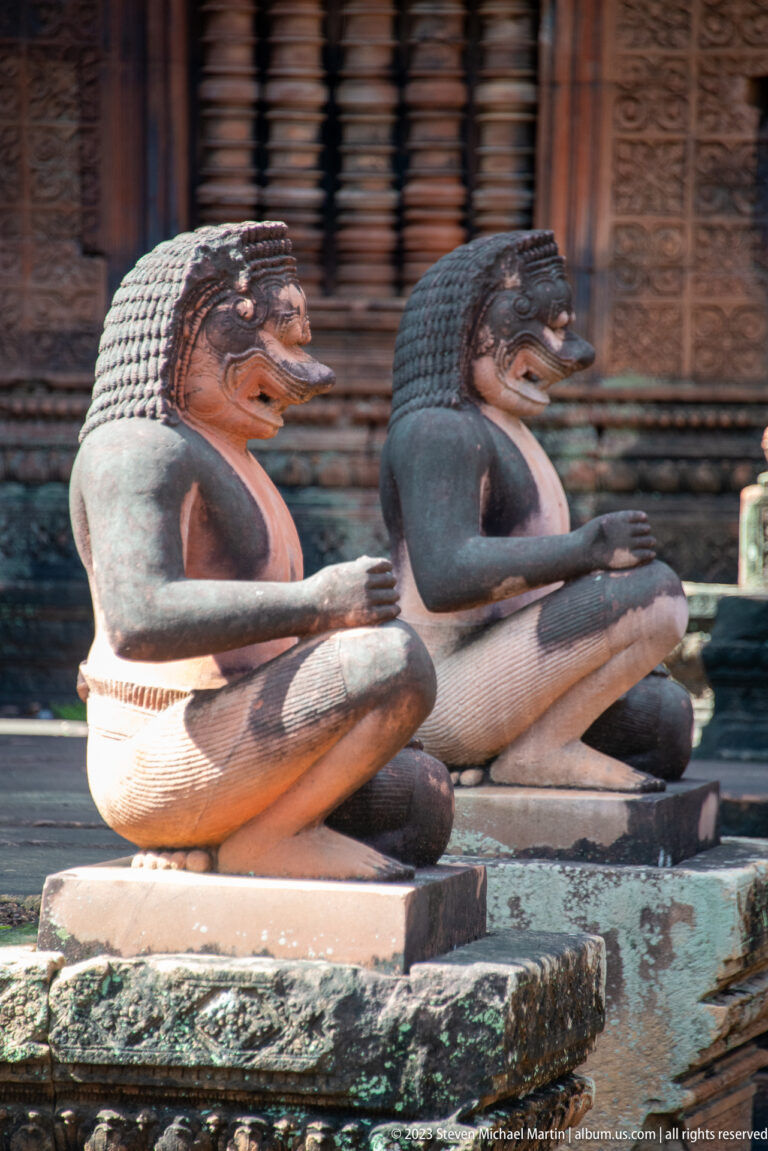 Two long-bodied guardian creatures in profile with raised torsos, open mouths, textured crests, and extended tails.