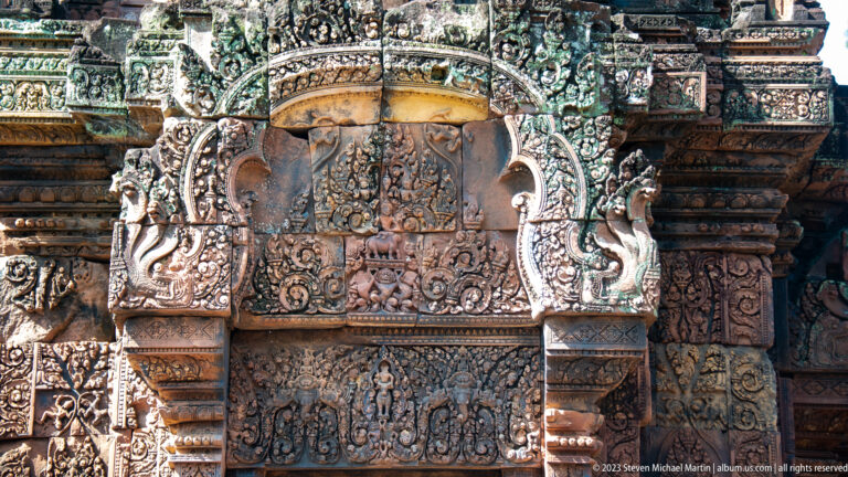 Close view of an ornate sandstone doorway crown with a central relief, flanking guardian creatures, and dense floral carving.