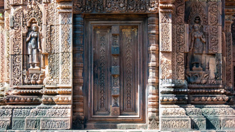 Closed temple doorway flanked by two standing female figures in carved sandstone niches.