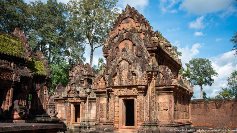 Three-quarter view of a compact pink-sandstone temple building with tall carved pediments and open doorways.