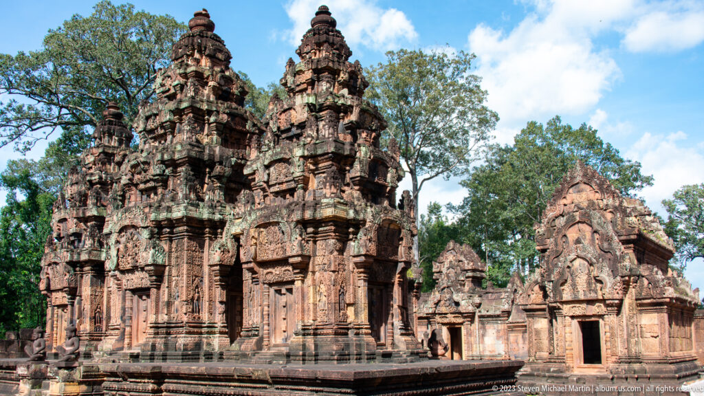 Three carved sandstone sanctuary towers beside a lower pedimented temple building under blue sky.