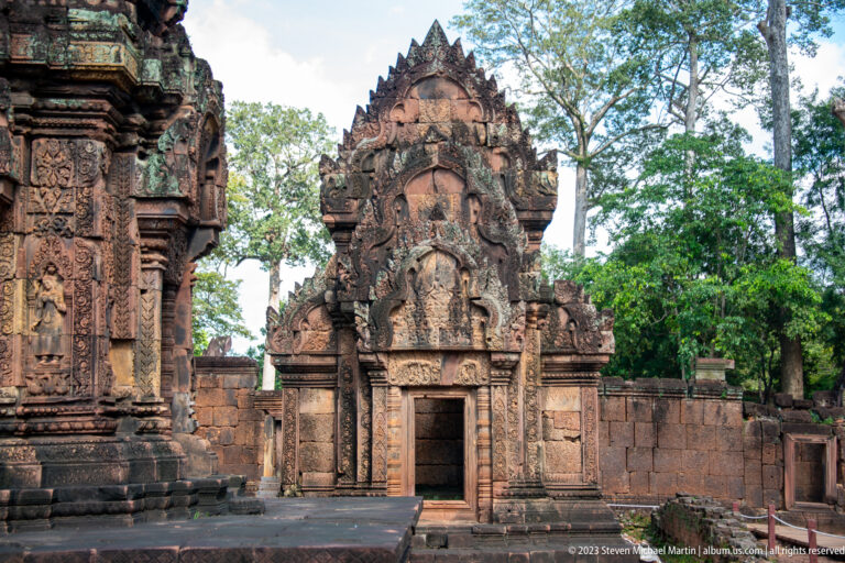 Frontal pink-sandstone temple building with a tall carved pediment and open central doorway.