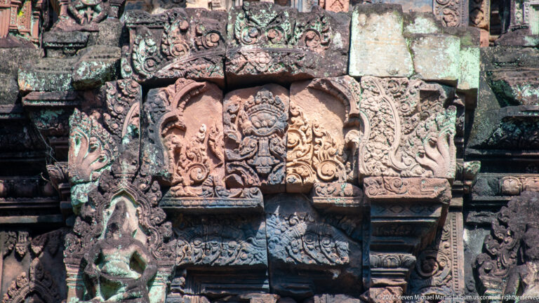 Central carved face surrounded by symmetrical foliage beneath a floral sandstone band.