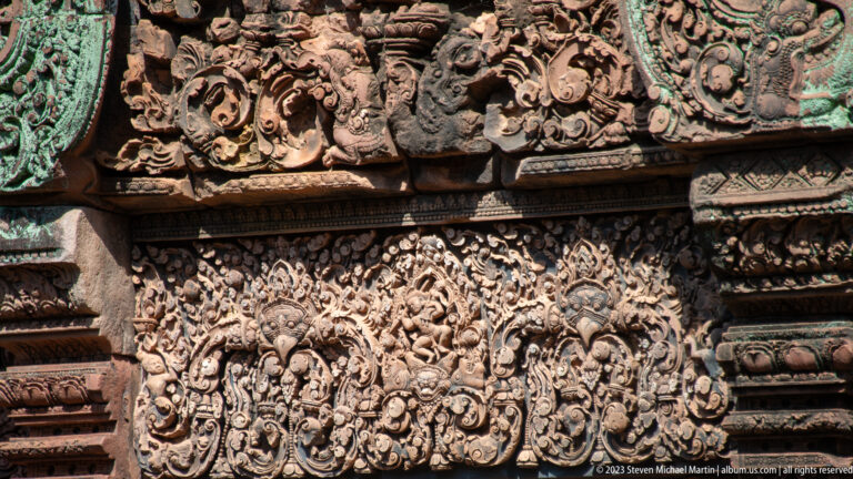 Broad sandstone lintel with a central sacred figure and dense symmetrical vegetal scrollwork.