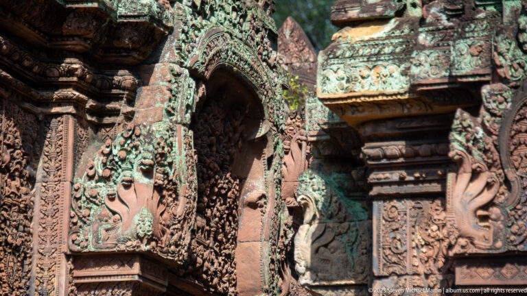 Angled close view of layered carved sandstone arches, pilasters, and projecting temple ornament.