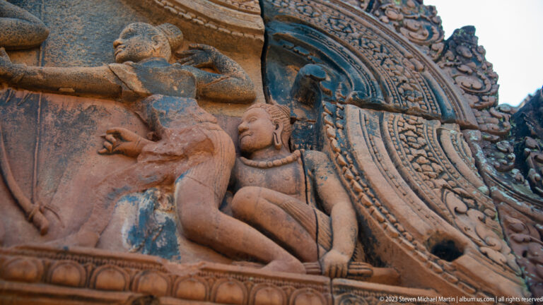 Close carved female figure leaning beneath the curved border of a sandstone pediment.