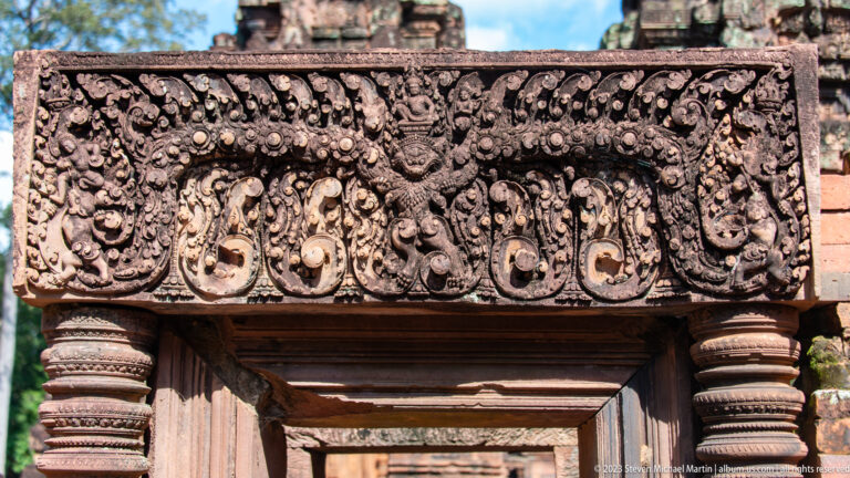 Carved sandstone lintel with a central face and curling foliage above a rectangular doorway.