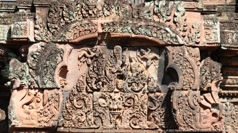 Large carved sandstone pediment with a central narrative scene, side figures, and curling ornament.