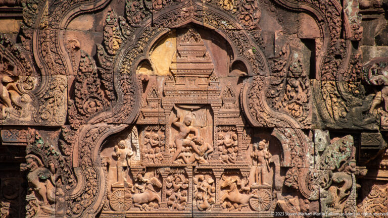Pointed sandstone pediment with a tiered palace façade above several rows of carved figures.