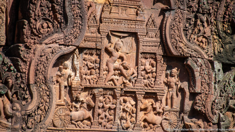 Close sandstone relief with a palace façade above crowded rows of people and animals.