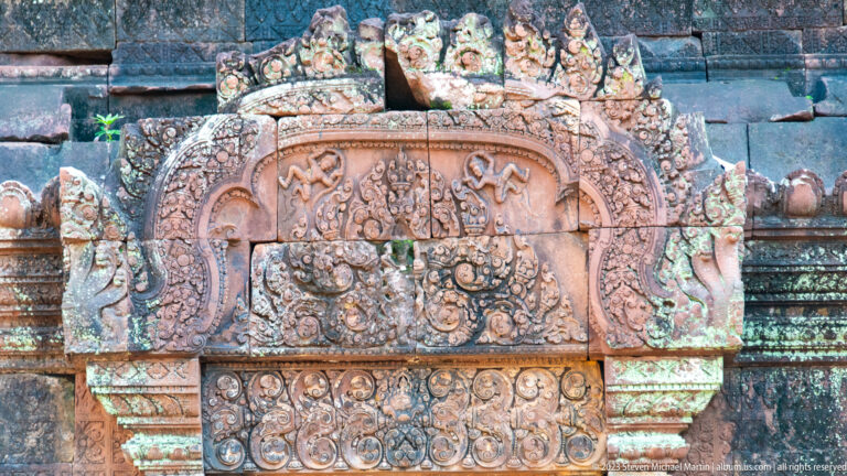 Frontal sandstone panel with an arched top, paired round masks, and a lower band of circular scrolls.