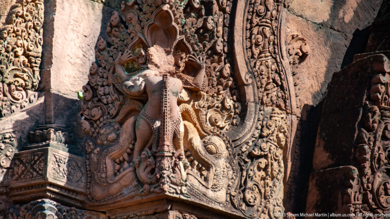 Standing crowned figure projecting from a sandstone corner beneath a carved ornamental hood.