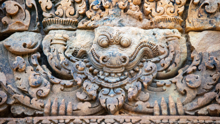 Frontal carved mask with bulging eyes, broad mouth, and symmetrical curling extensions.