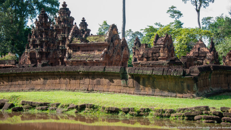 Temple towers and pedimented buildings rising closely behind a long sandstone enclosure wall.
