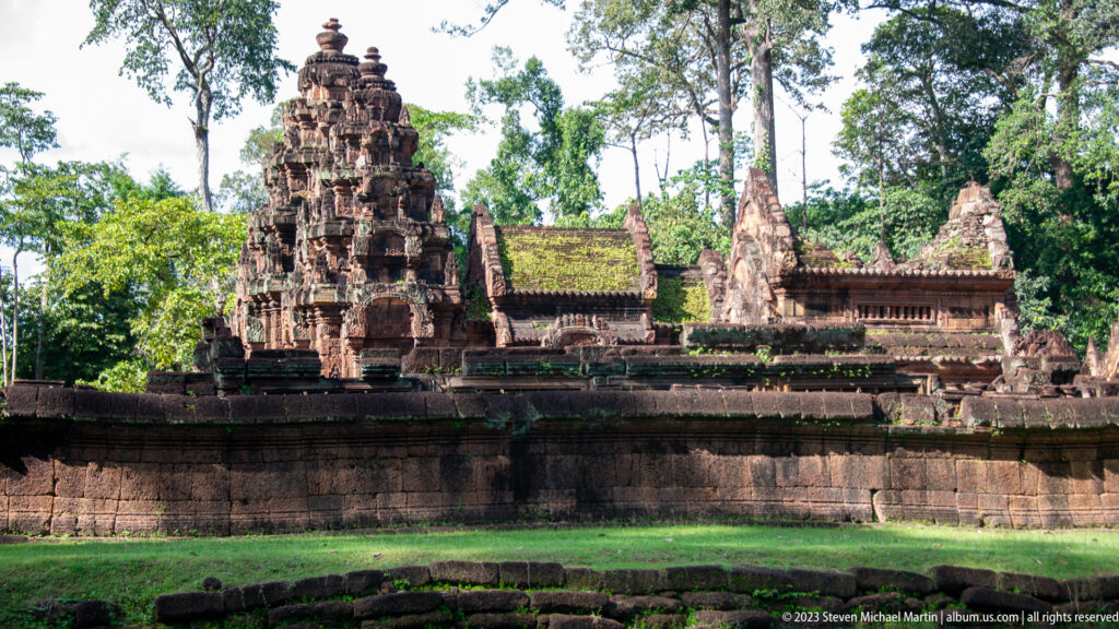 Closer exterior view of Banteay Srei's carved central sanctuary tower, adjoining pediments, and sandstone enclosure wall.
